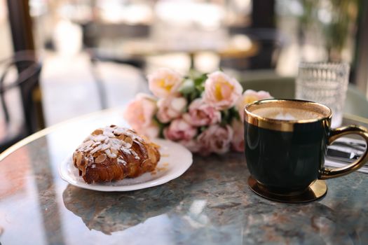 Elegant café setting with cappuccino, croissant, and flowers on a marble table.