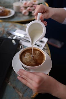 A person adding milk to a coffee cup on a table, creating a perfect morning beverage.