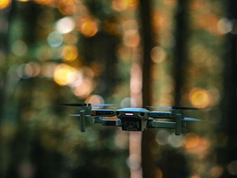 A drone flying amid a forest backdrop with a soft bokeh effect, showcasing modern technology.