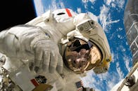 This picture shows an american astronaut in his space and extravehicular activity suite working outside of a spacecraft. In the background parts of a space shuttle are visible. In the far backgroun...