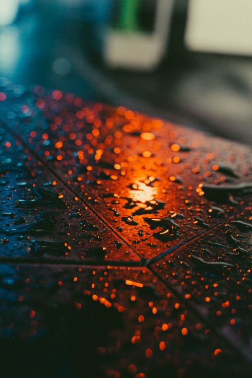 Free Close-up of raindrops reflecting city lights on a wet surface, capturing moody ambiance. Stock Photo