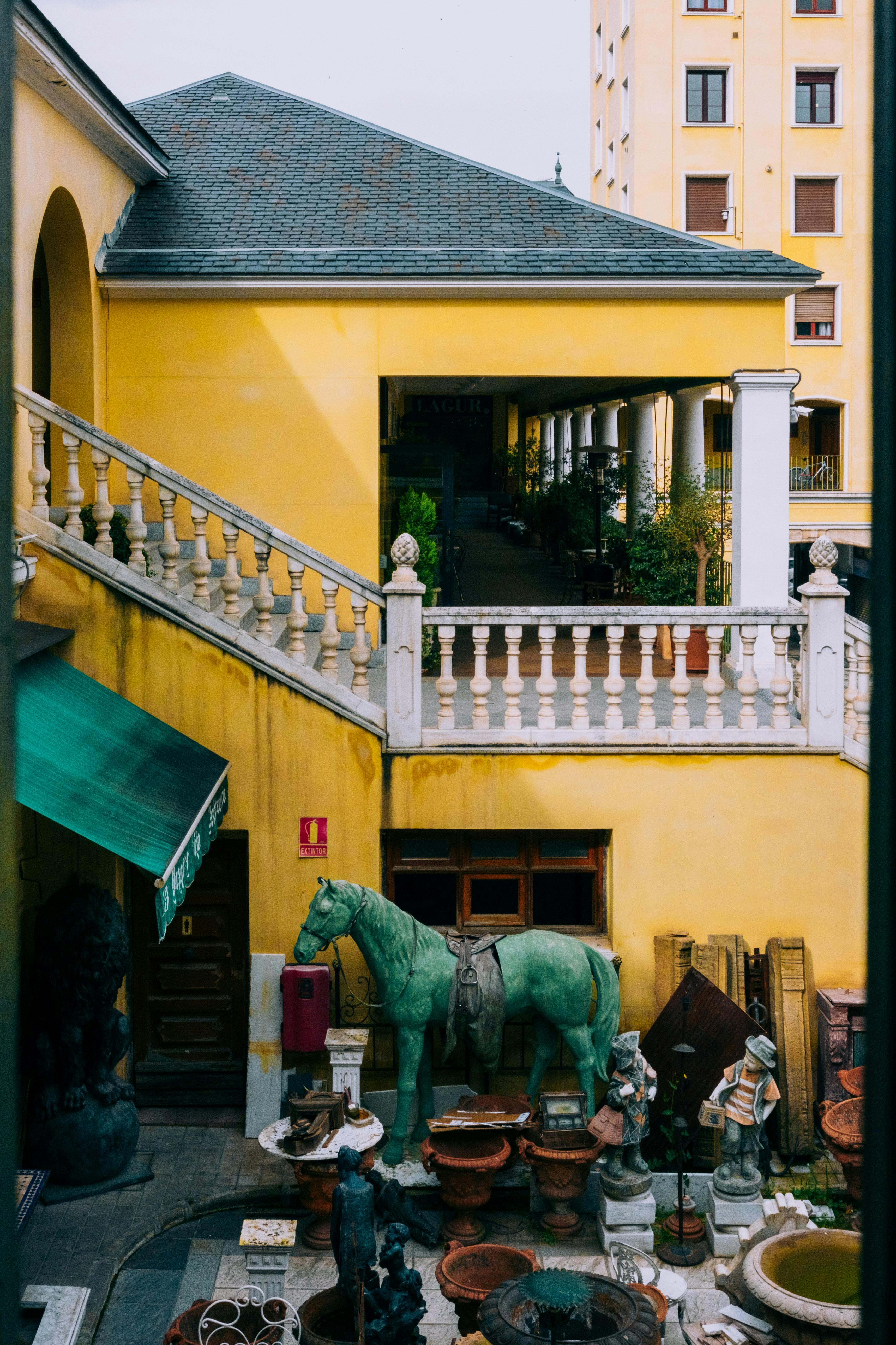 Explore a vibrant courtyard in Madrid, showcasing yellow architecture, statues, and greenery.