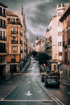 Street in Madrid with iconic buildings and dramatic overcast sky, showcasing urban life.