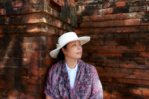 女人穿着白色的帽子，斜倚在棕色的墙上