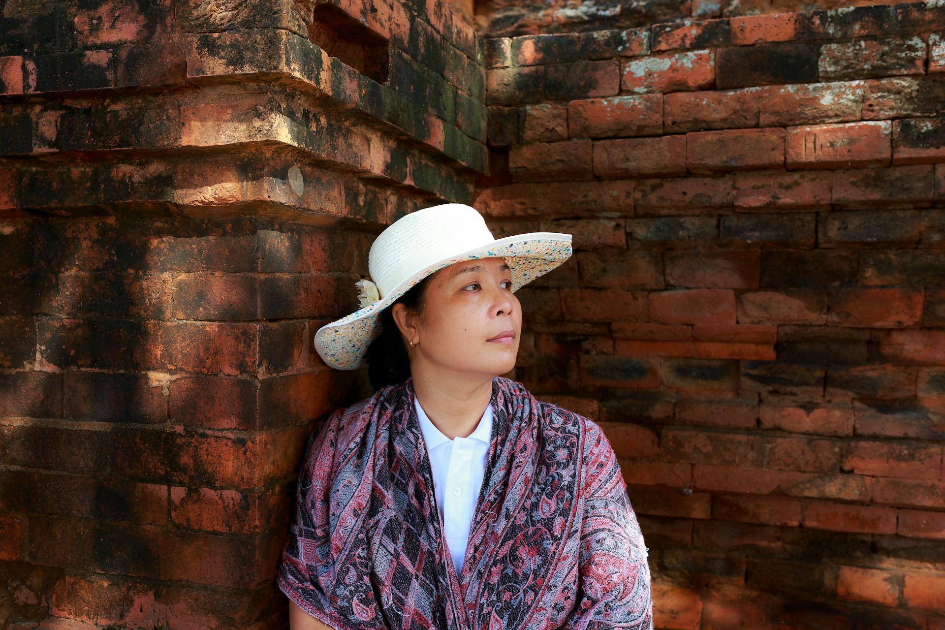 Woman Wearing White Hat Leaning on Brown Wall