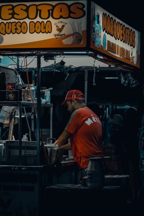 A man in a red shirt is standing in front of a food stand