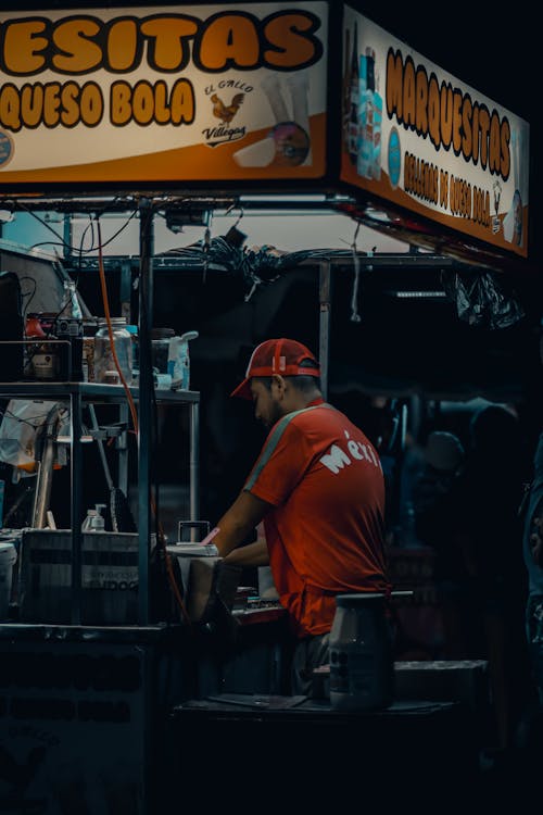 Free A man in a red shirt is standing in front of a food stand Stock Photo