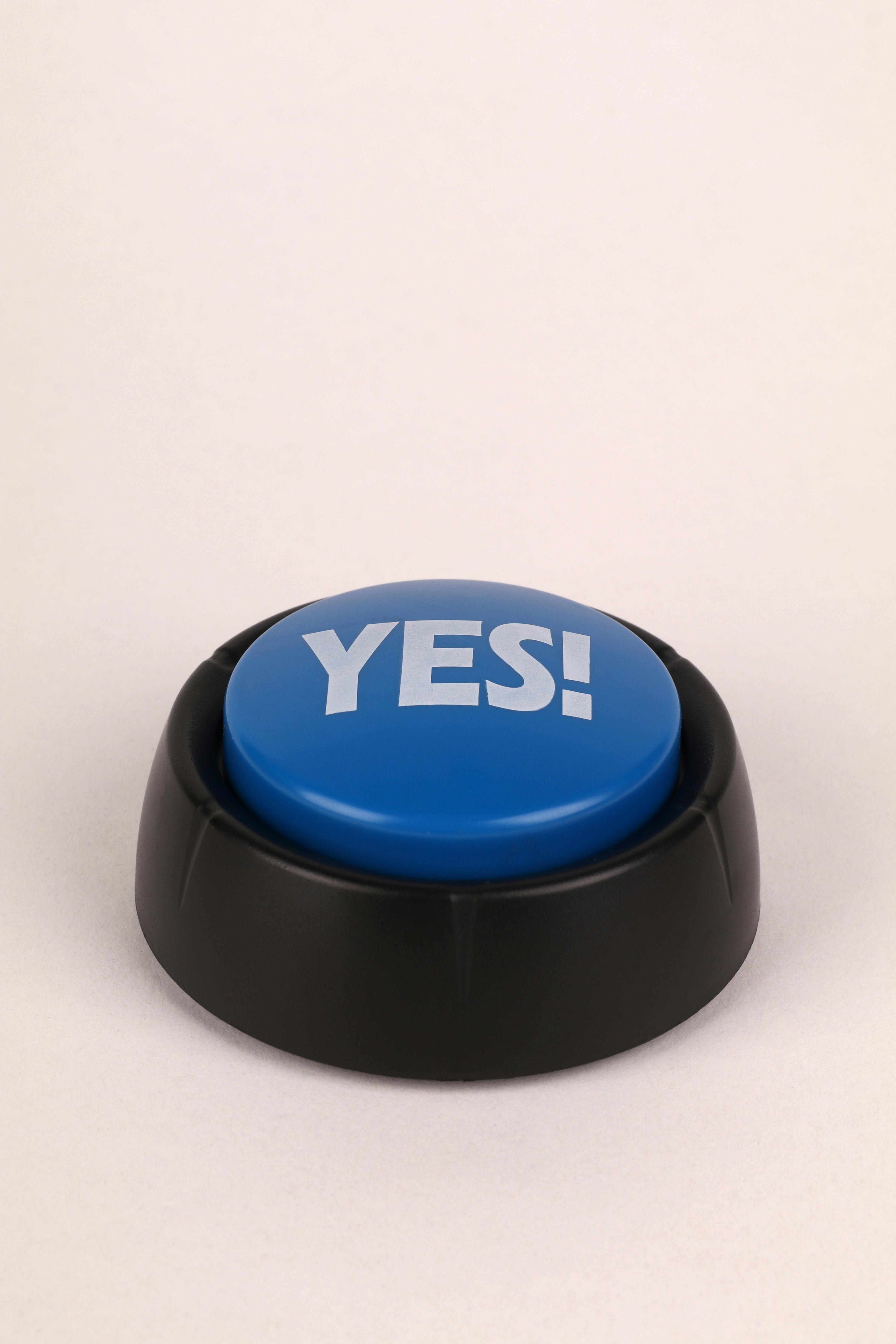 A blue yes button with black base on a beige background, perfect for communication concepts.