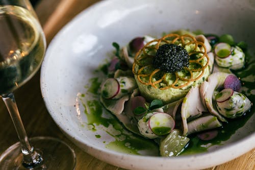 A white bowl with food and a glass of wine