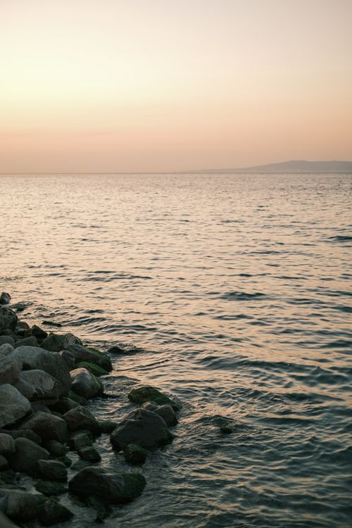 Free Peaceful sunset view over a rocky coastal shoreline with calm sea waves. Stock Photo