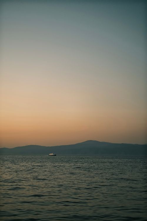 Free A peaceful sunset over the ocean with a distant ship on the horizon, offering solitude and calm. Stock Photo
