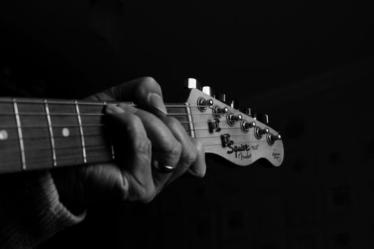 Close-up shot of a hand playing a guitar in a dark studio setting, evoking a musical ambiance.