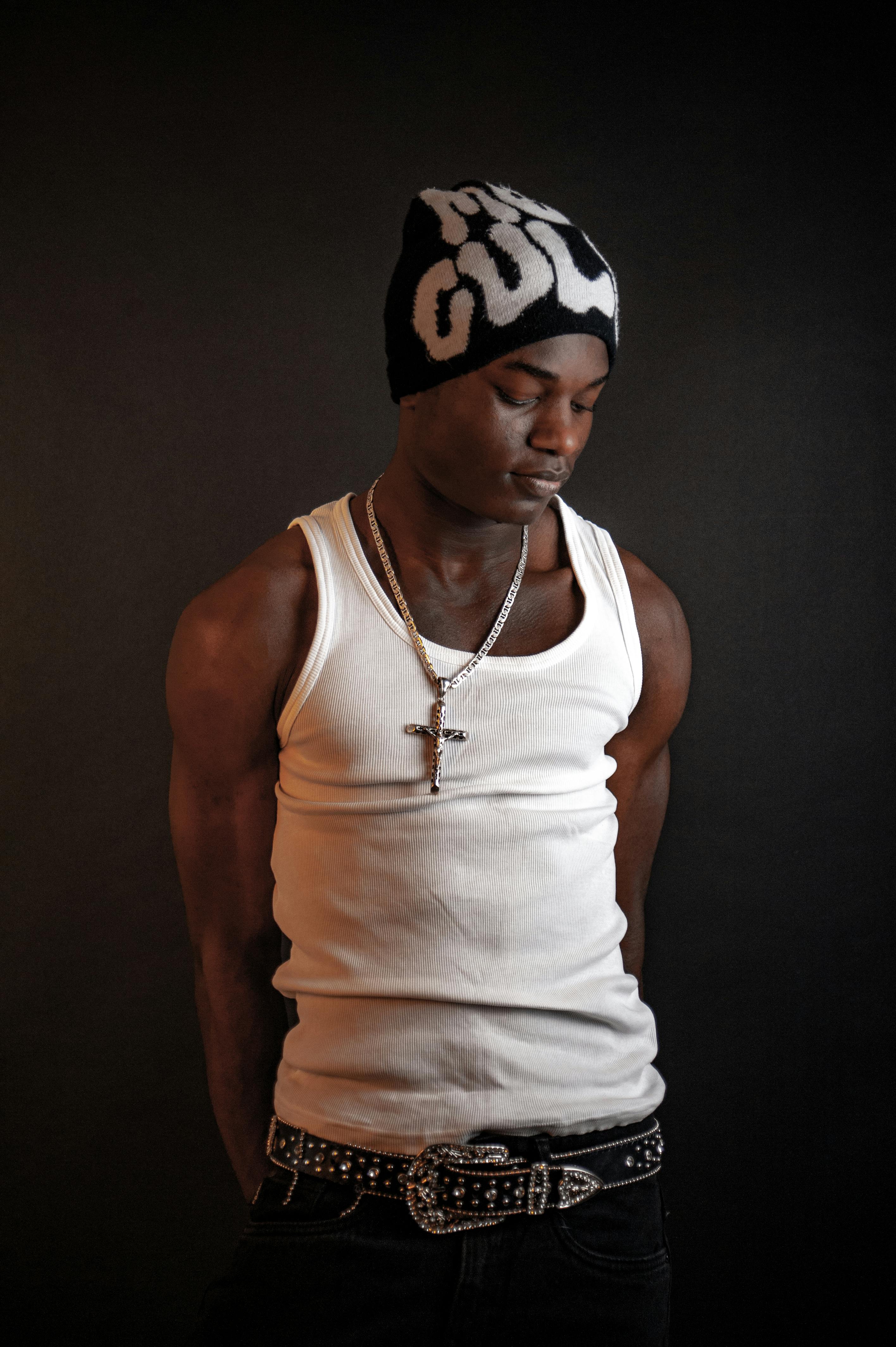 Portrait of a man in studio with beanie, necklace, and ornate belt on a dark background.