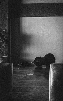 Monochrome photo of a cello lying on the floor in an empty room, creating a mysterious ambiance.
