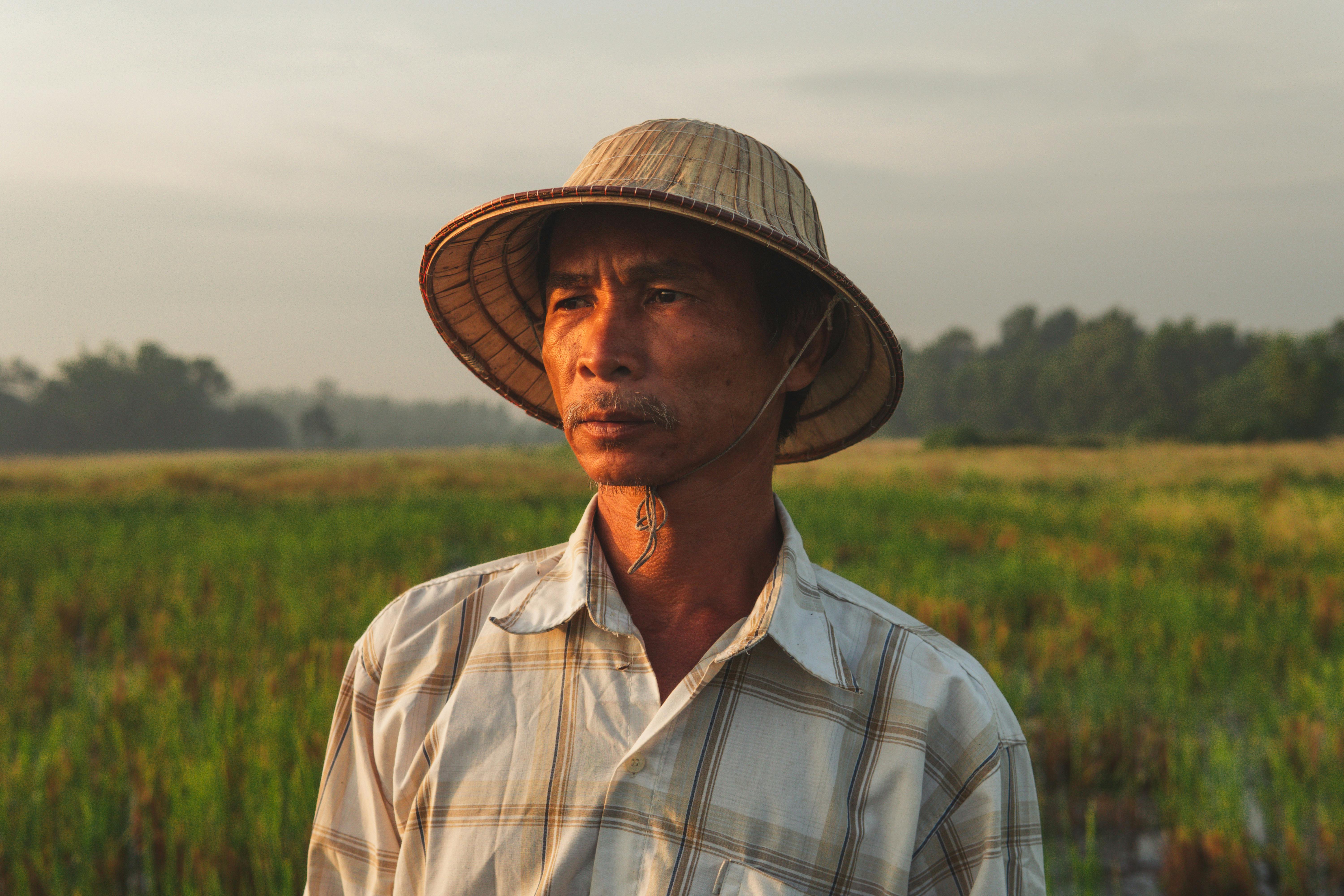 Portrait of a farmer in a straw hat standing in a rural field at sunrise.