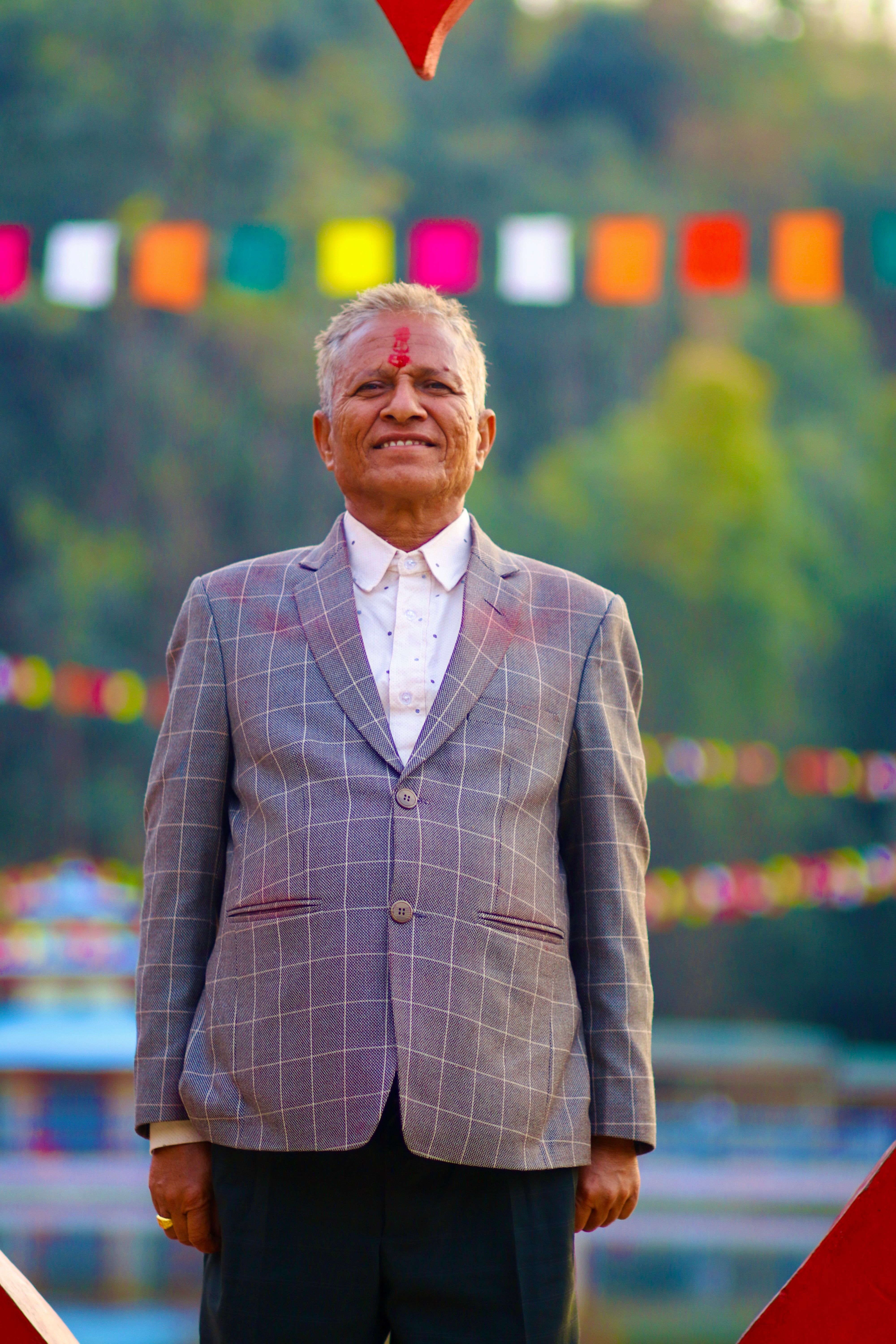 Senior man joyfully celebrating Holi festival outdoors with colorful decorations in the background.