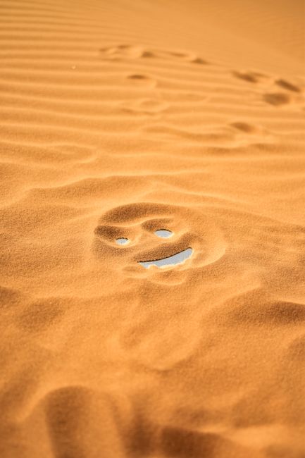 A playful smiley face drawn in the sand amidst the Algerian desert dunes.