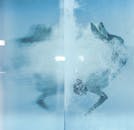 一个人在清澈的蓝色水池中，带着气泡在水下游泳，捕捉着运动和光线的反射