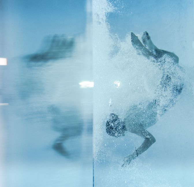 Person swimming underwater with air bubbles in a clear blue pool. Captures motion and light reflections.