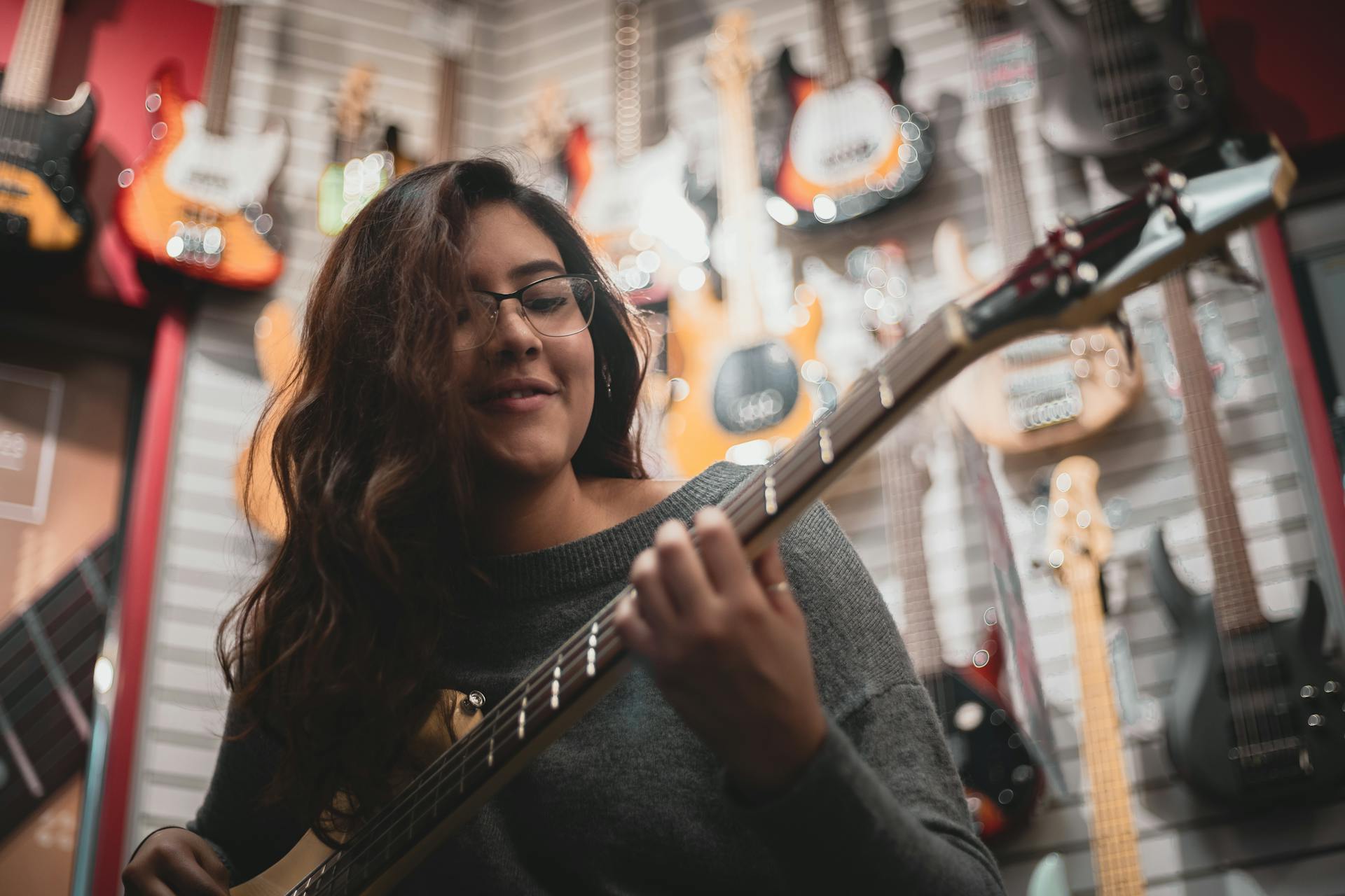 A woman enjoys playing guitar surrounded by musical instruments in a vibrant store setting.