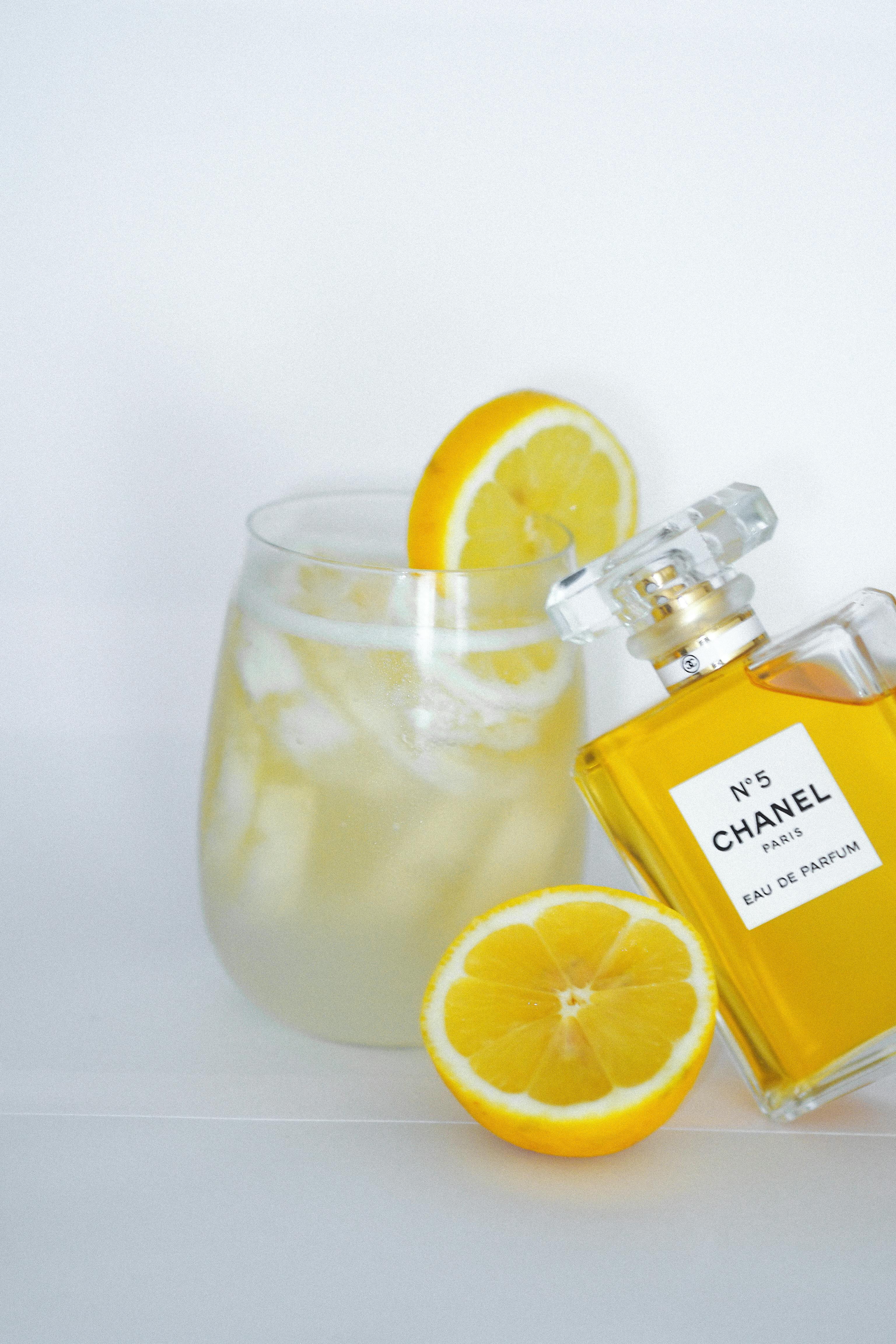 Chanel No.5 perfume bottle next to a lemonade with lemon slices on white background.
