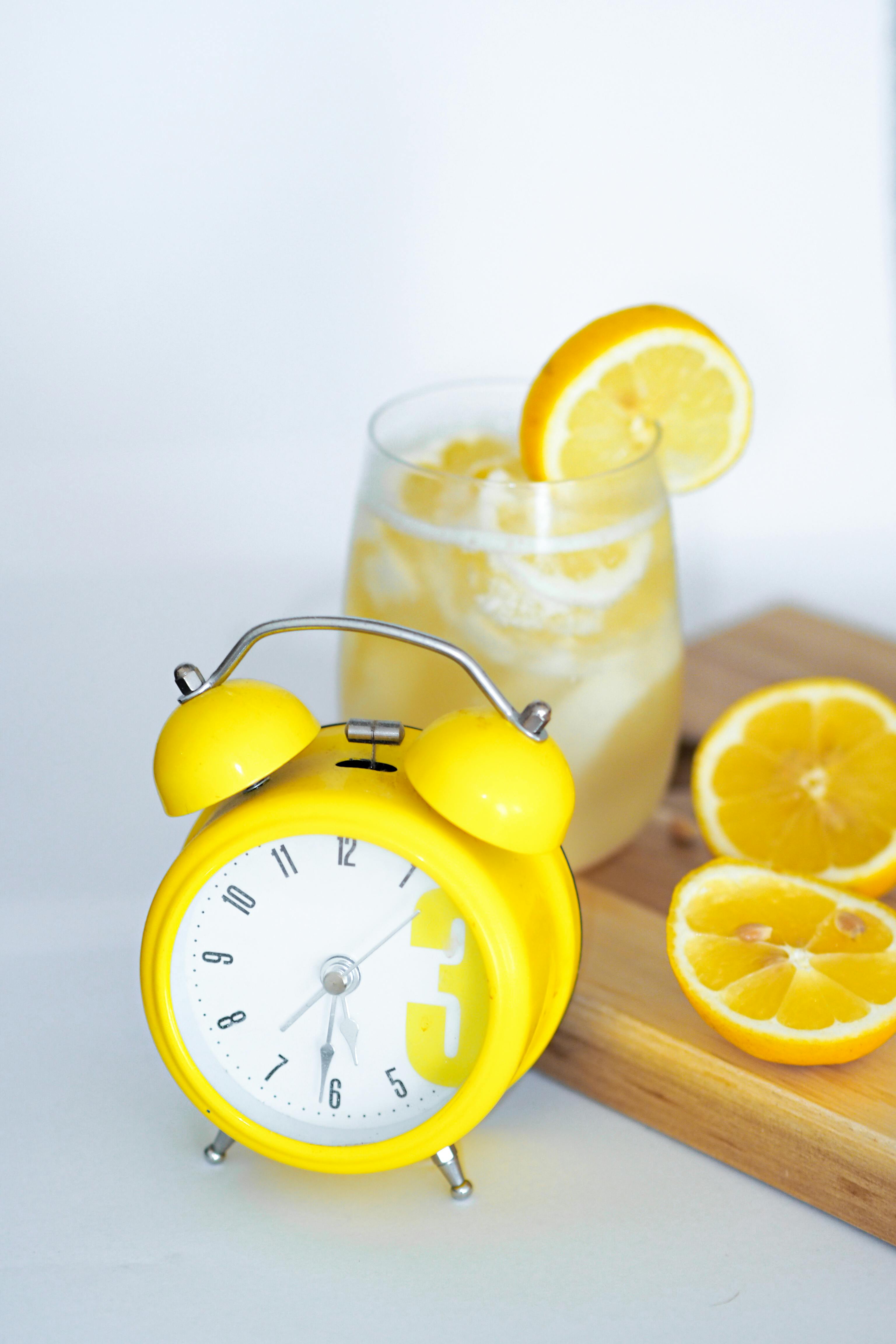 A fresh lemon drink with a bright yellow alarm clock on a wooden board.