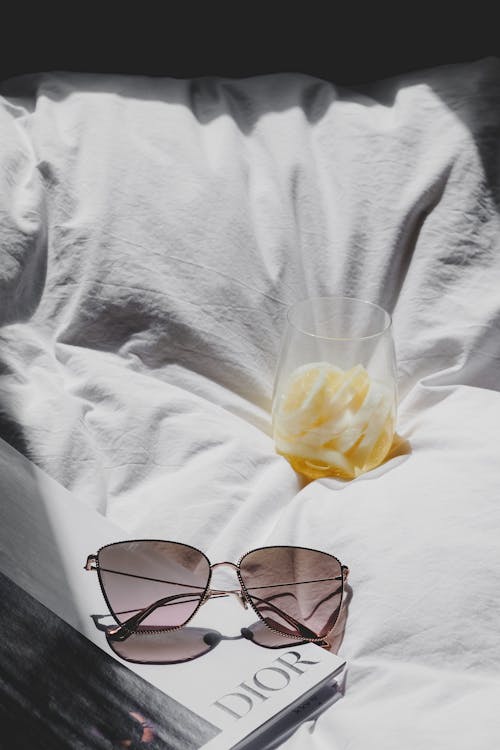 Free A book, sunglasses and a glass of orange juice on a bed Stock Photo