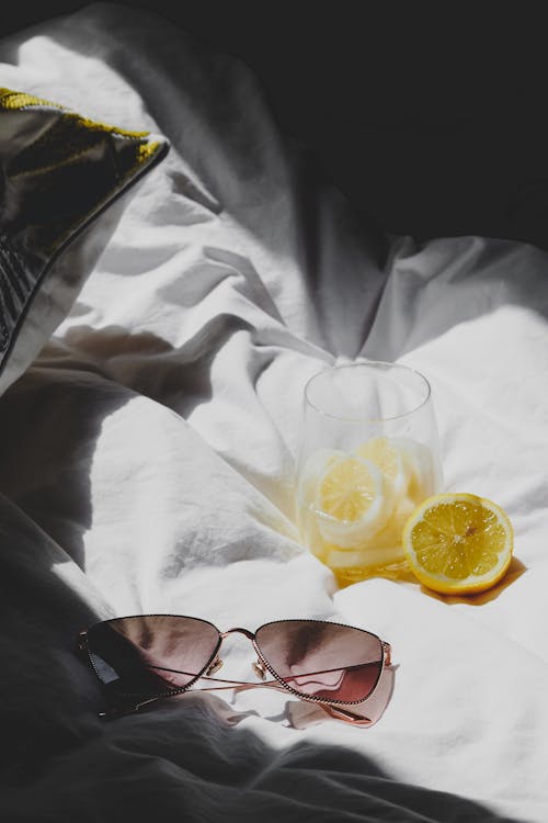 A pair of sunglasses and a lemon on a bed