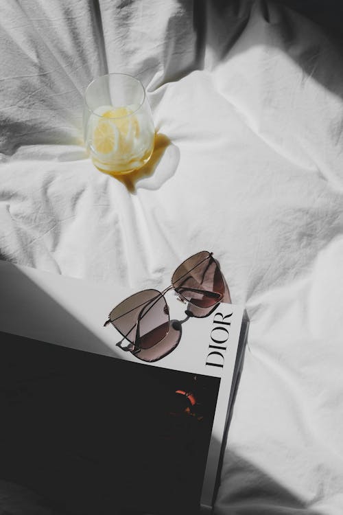 A book, sunglasses and a glass of orange juice on a bed