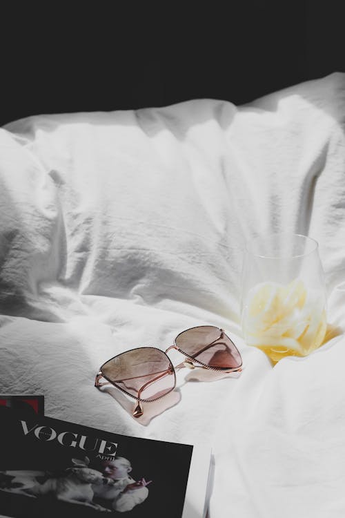 A book, sunglasses and a magazine on a bed