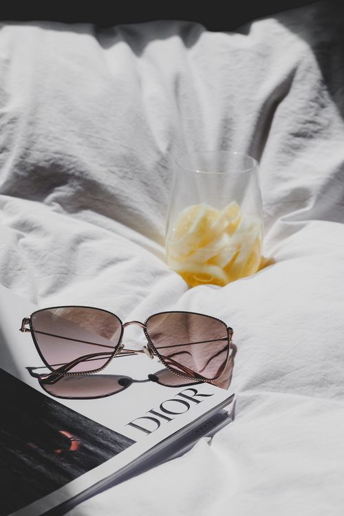 Free Sunglasses and a refreshing drink on a Dior magazine in soft sunlight, evoking a luxurious and relaxed vibe. Stock Photo