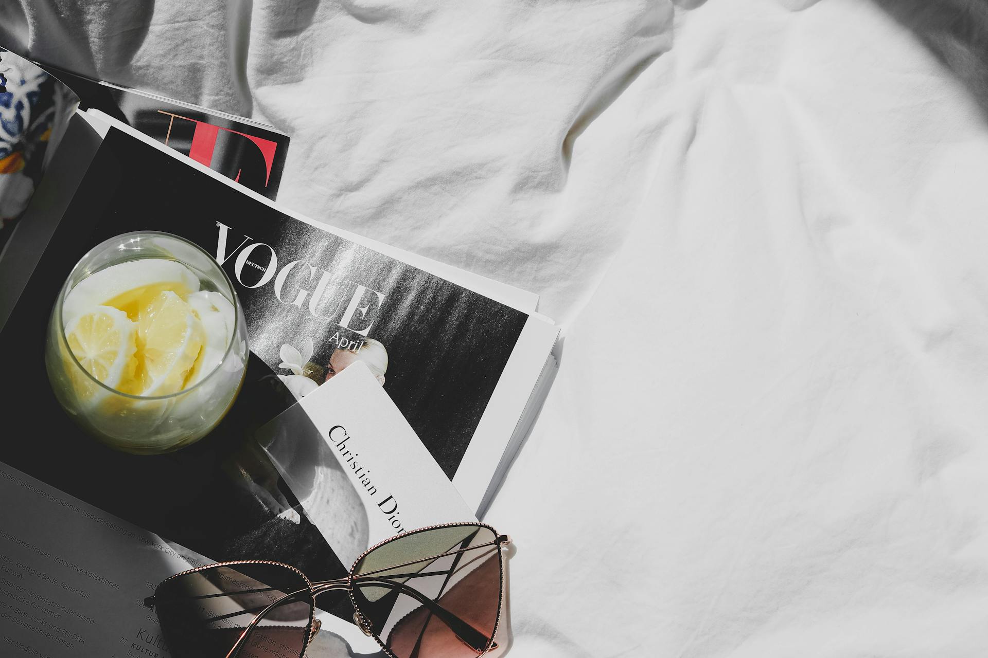 Luxurious still life featuring Dior, Vogue, sunglasses, and lemonade on white fabric in Paris.