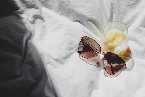 Free A pair of sunglasses and a glass of orange juice on a bed Stock Photo