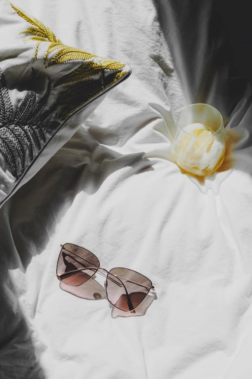 A pair of sunglasses laying on a bed with a flower