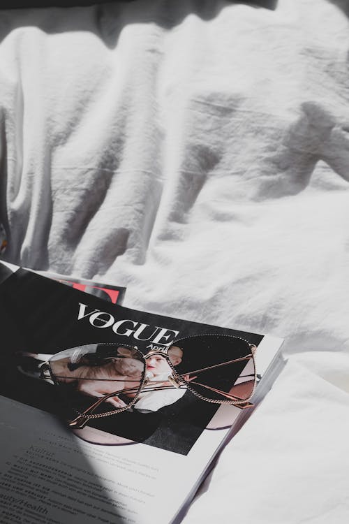 A magazine on a bed with glasses and a book