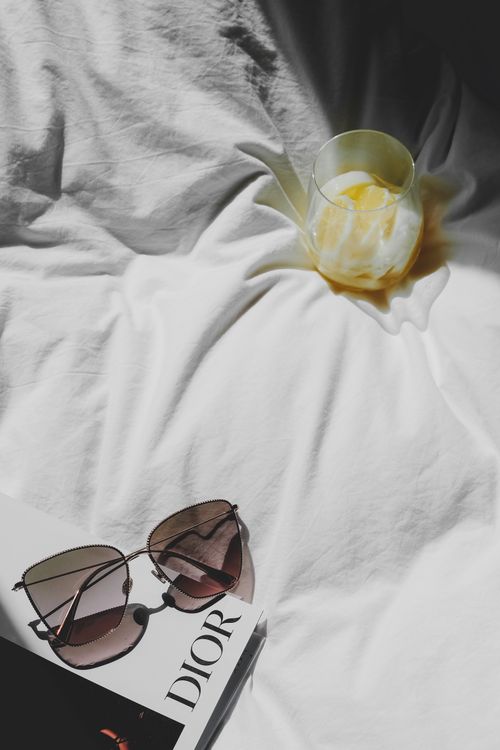 Free Glamorous sunglasses and a refreshing drink on a sunlit bed with a stylish magazine, capturing elegance. Stock Photo