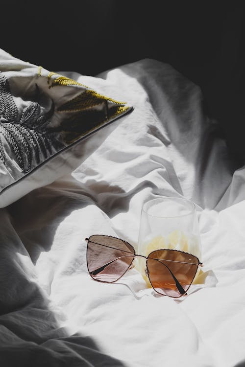 A pair of sunglasses and a glass of juice on a bed