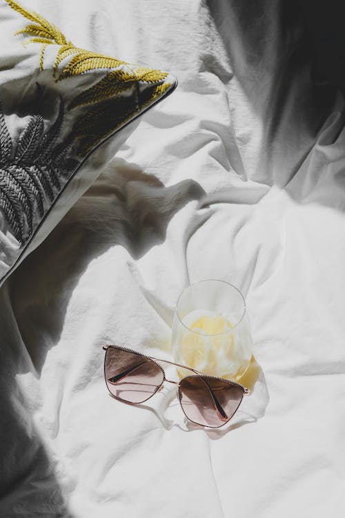 Free A pair of sunglasses and a drink on a bed Stock Photo