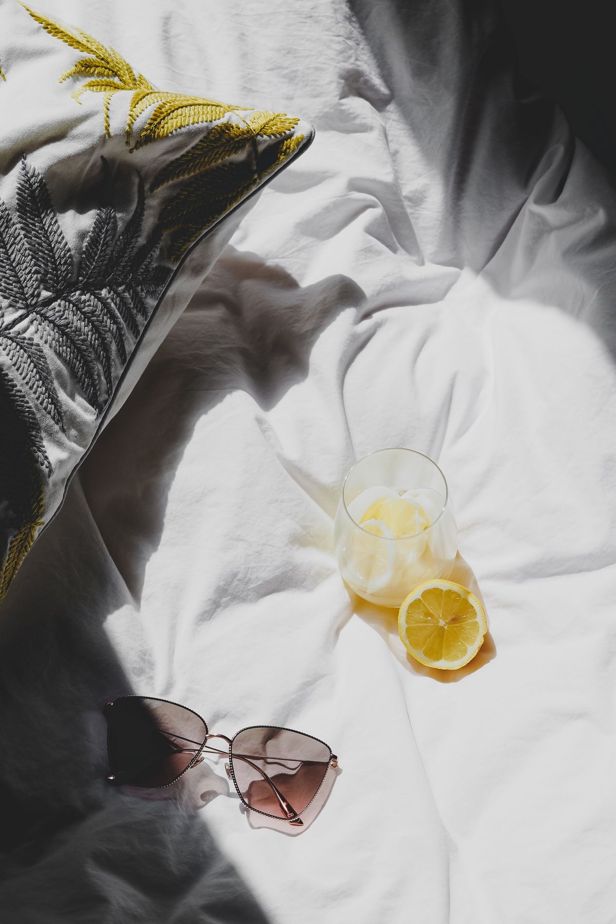 A cozy morning scene with lemons and sunglasses in sunlight on a bed. Stock Photo.