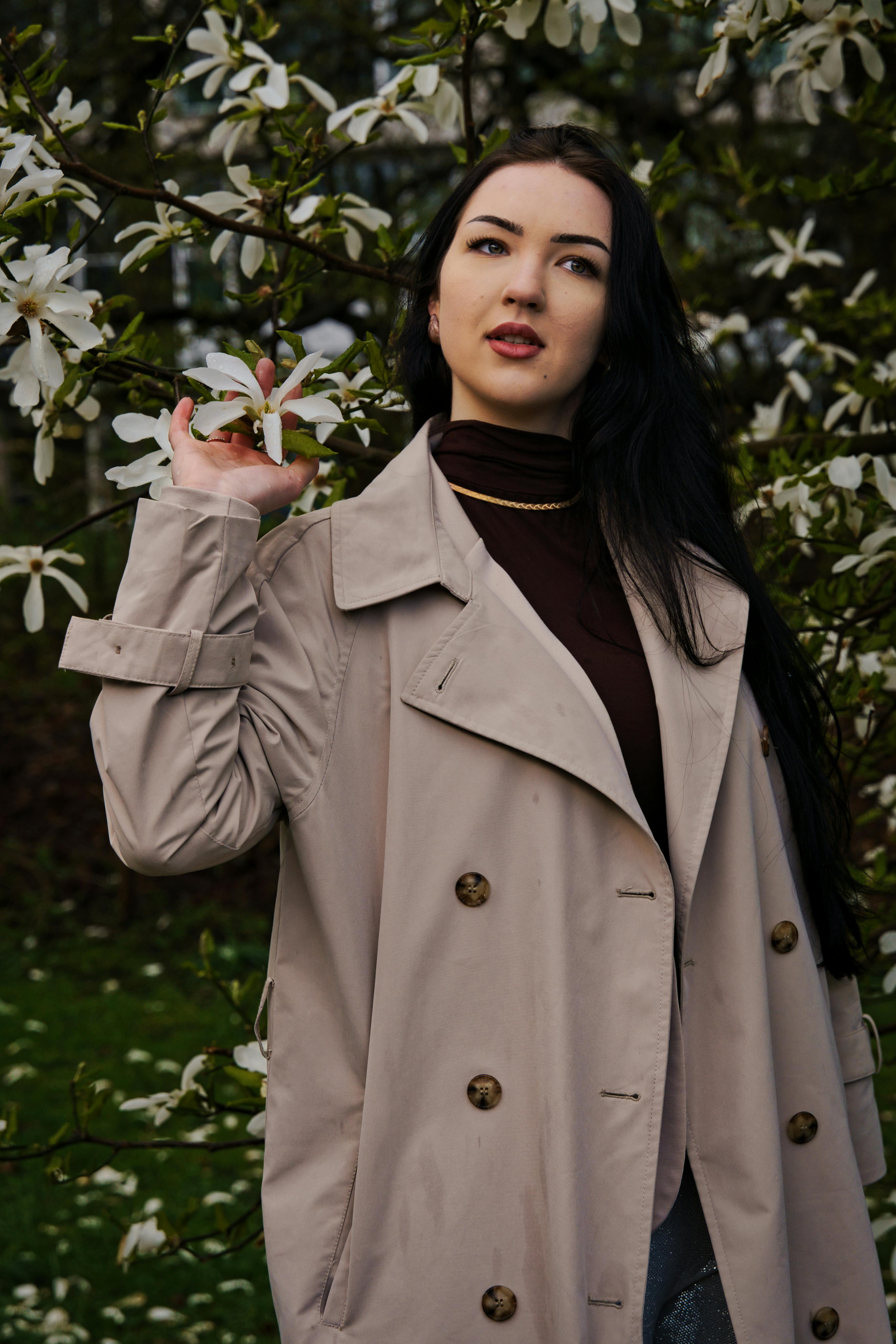 brunette in coat posing with flowering shrub