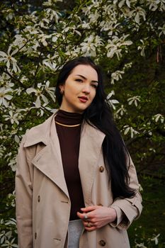 Fashionable woman poses in a beige coat among blooming white flowers outdoors in Bremen.