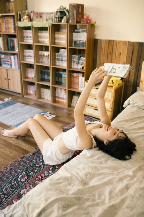 Free A young woman comfortably reads a book while relaxing in a cozy room filled with bookshelves. Stock Photo