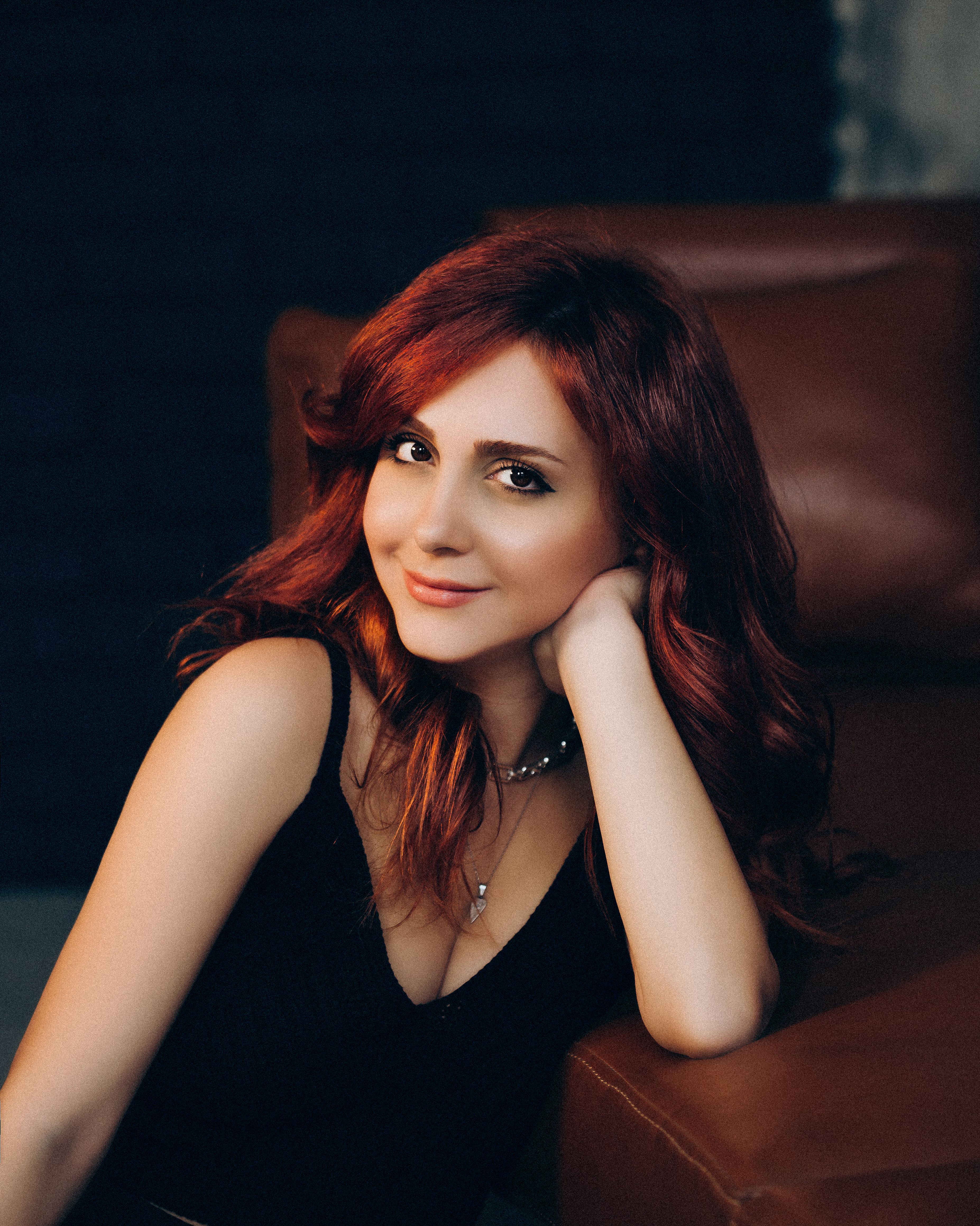 Elegant redhead woman posing indoors with a warm smile and stylish attire, shot in Baku, Azerbaijan.