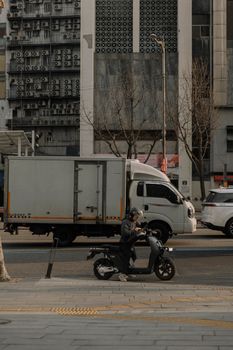 A dynamic urban street scene with a man on a scooter near a truck and modern architecture.
