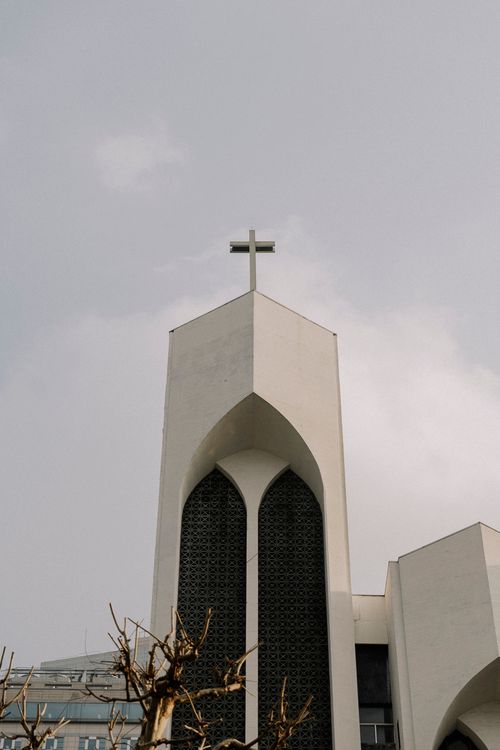 Free A contemporary church tower featuring a cross and arched windows under a cloudy sky. Stock Photo