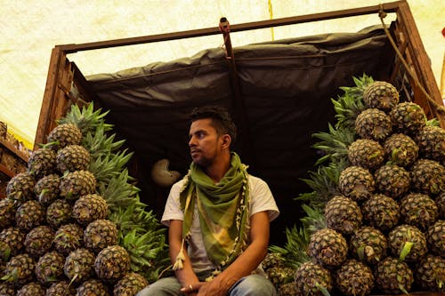 A man sitting on top of a pile of pineapples