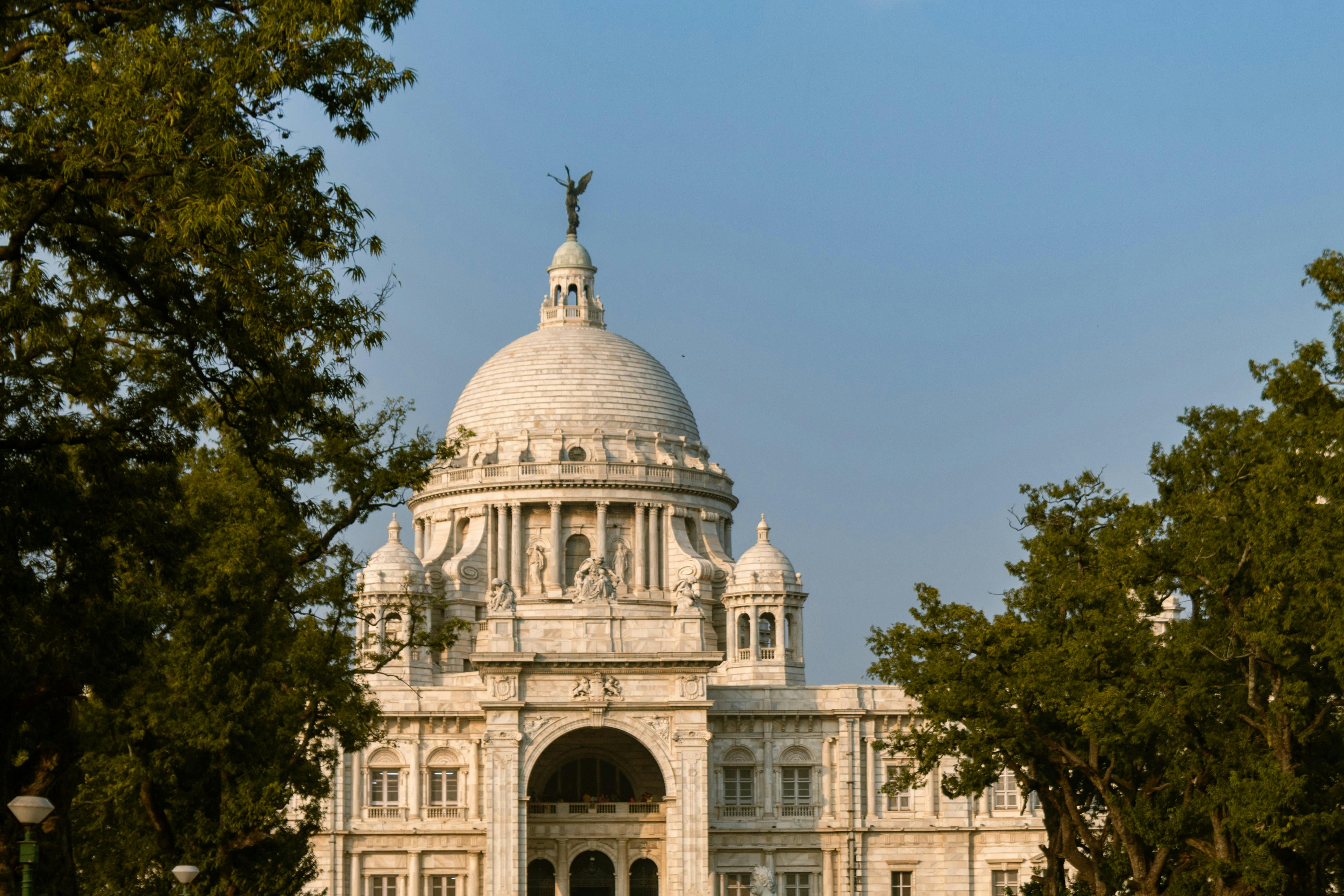 A majestic view of the Victoria Memorial in Kolkata, framed by lush green trees under a clear blue sky.