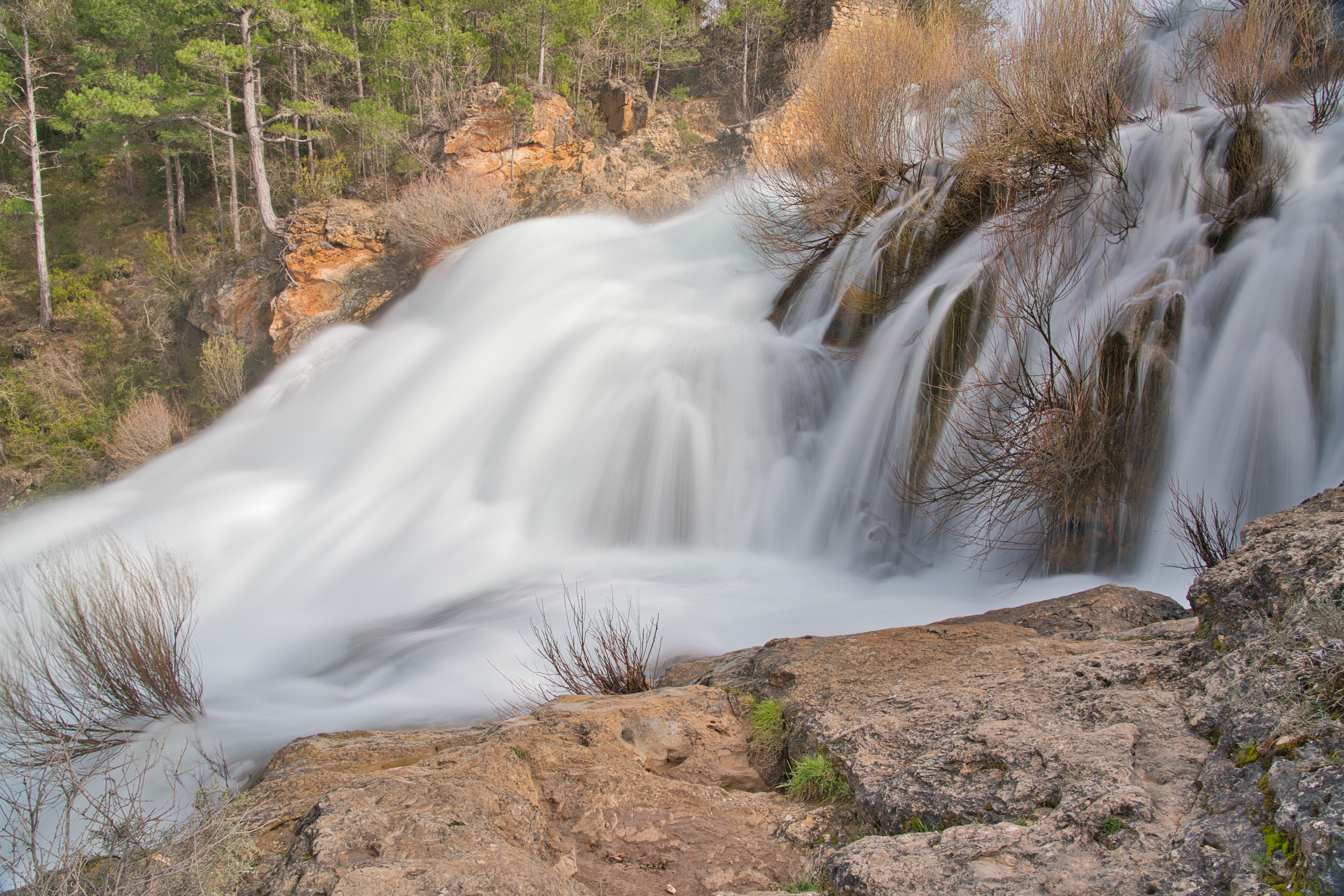 Beautiful long exposure of a waterfall in Guadalajara, Spain, surrounded by lush green trees.