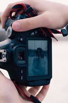 Hands holding a DSLR camera capturing a live view screen outdoors.