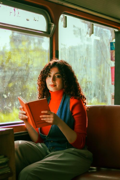 Free A young woman with curly hair reads a book on a bus, enjoying a quiet moment of relaxation. Stock Photo